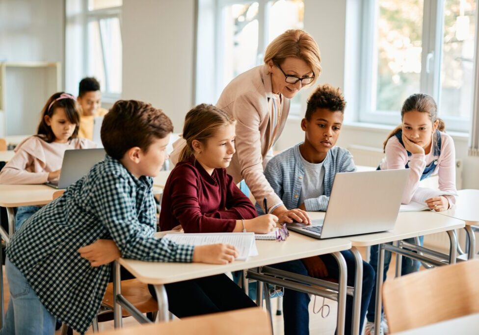 Elementary teacher and her students using laptop during computer class at school.